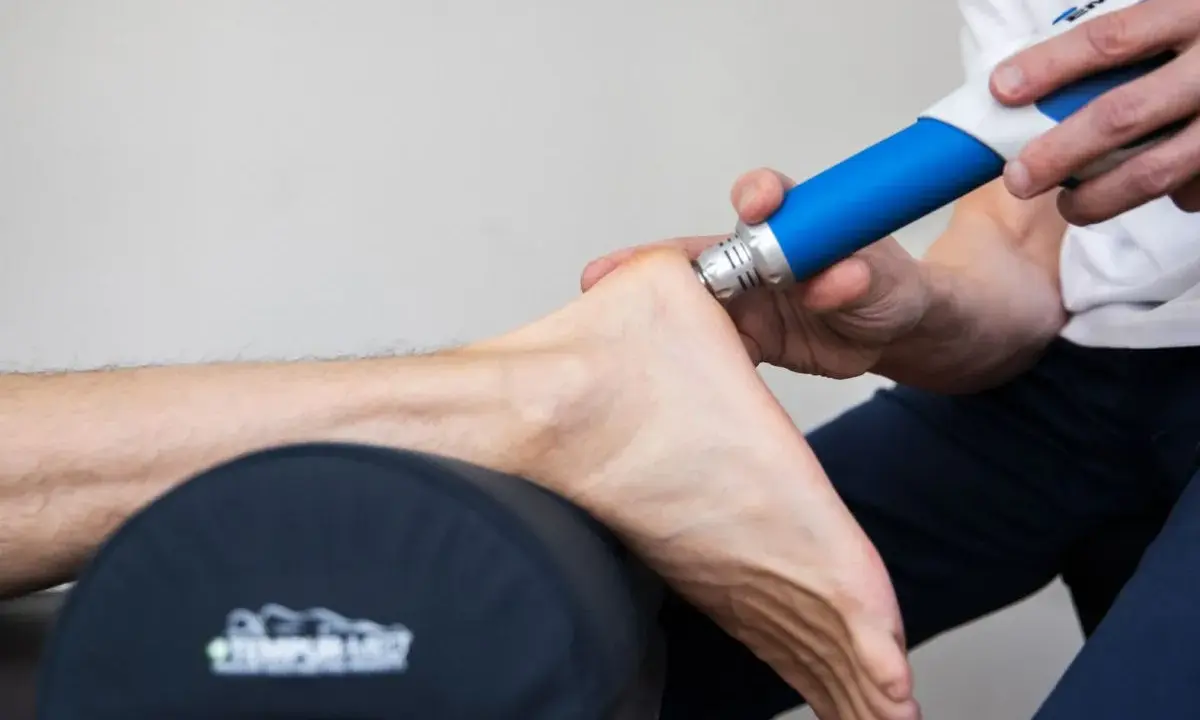 Behandling av plantar fasciit med stötvågsbehandling. En terapeut använder en blå enhet för att behandla en fot.