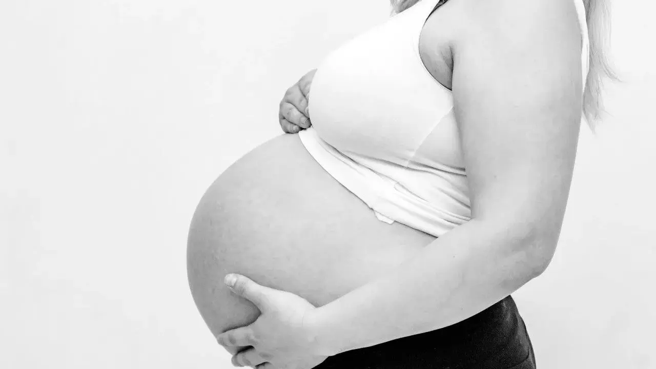 Gravid mage med händer som stöttar. Kanske ont i ljumsken gravid?