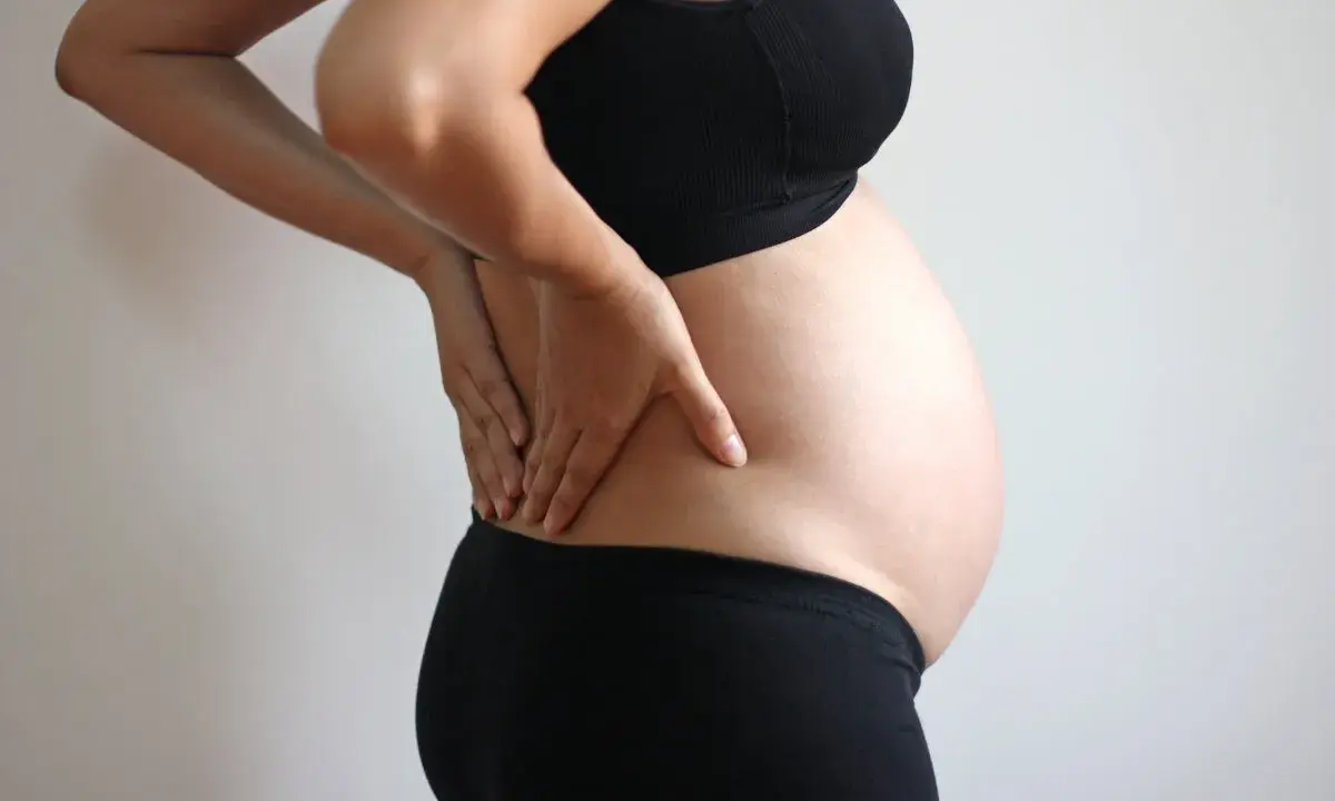Gravid kvinna med händerna på ryggen, upplever smärta som kan liknas vid analkramp.
