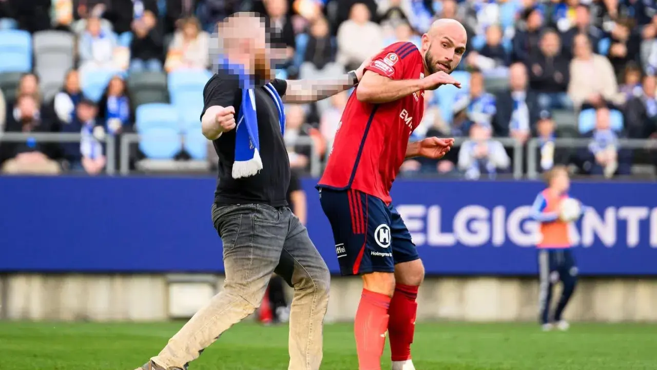 En åskådare ger en fotbollsspelare ett hårt slag mot hakan på planen.