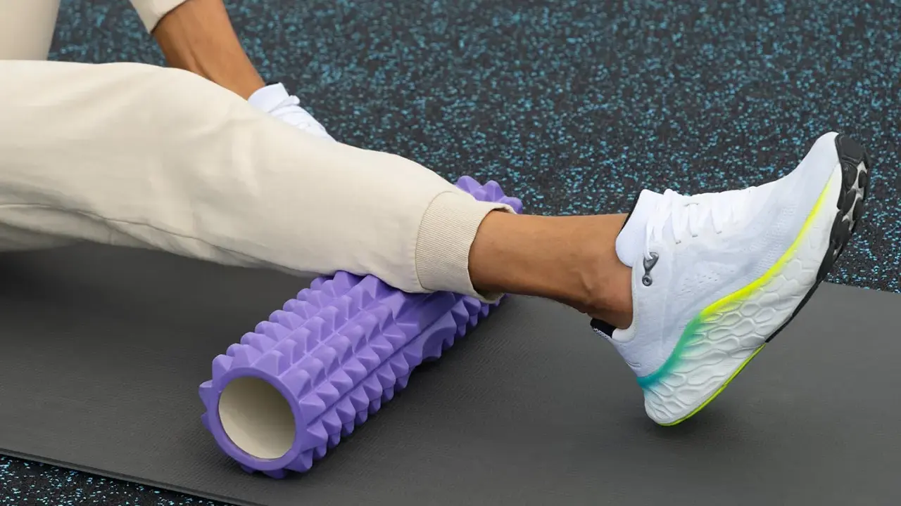 Person använder en lila foam roller rygg för att stretcha benet på en träningsmatta.