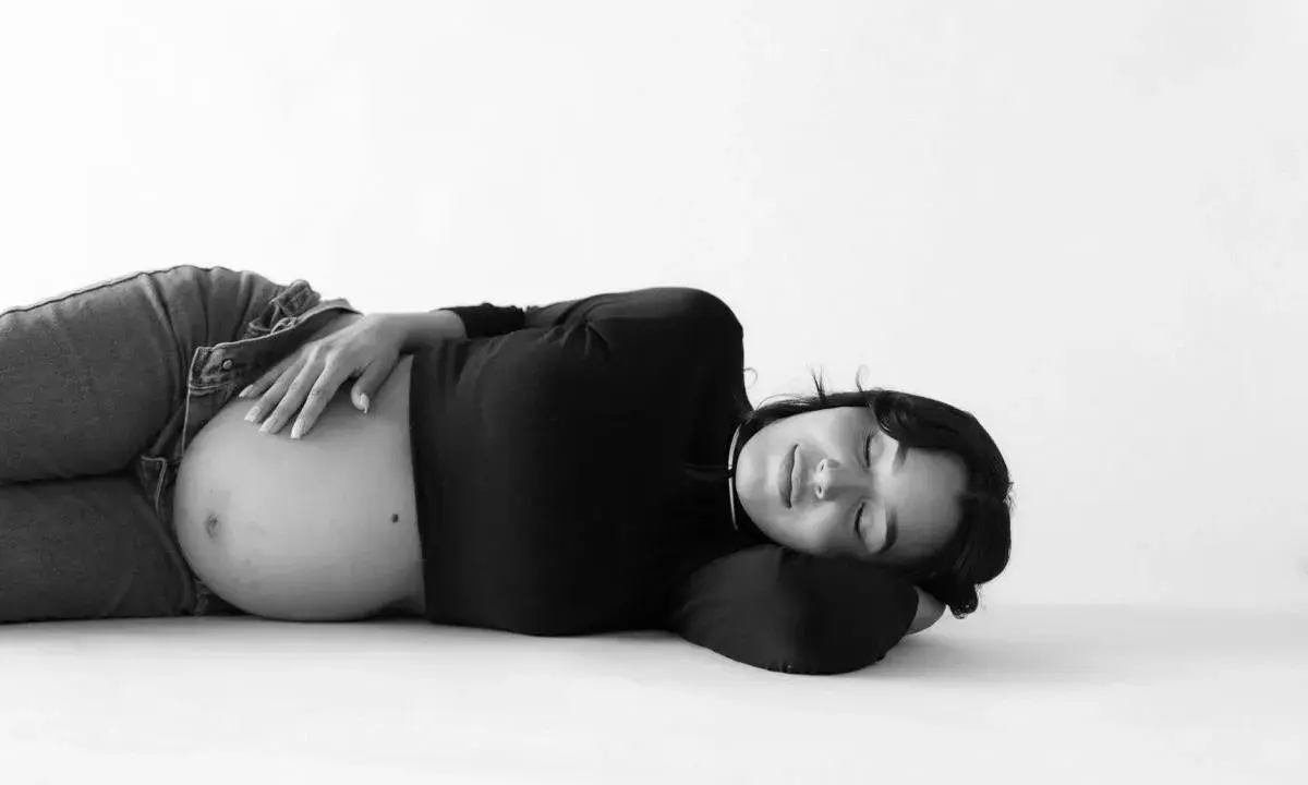 Gravid kvinna ligger på rygg, med handen på sin mage. Hon ser ut att vila.