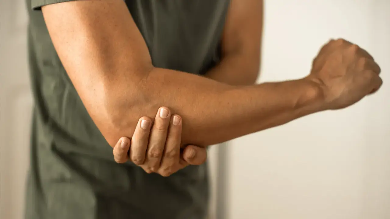 Person håller om sin armbåge, som om den har ett avslitet ledband.