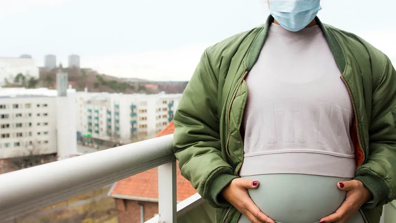 Gravid kvinna med munskydd på balkongen, omgiven av stadens silhuett. Känns det som att du är oftare sjuk gravid?