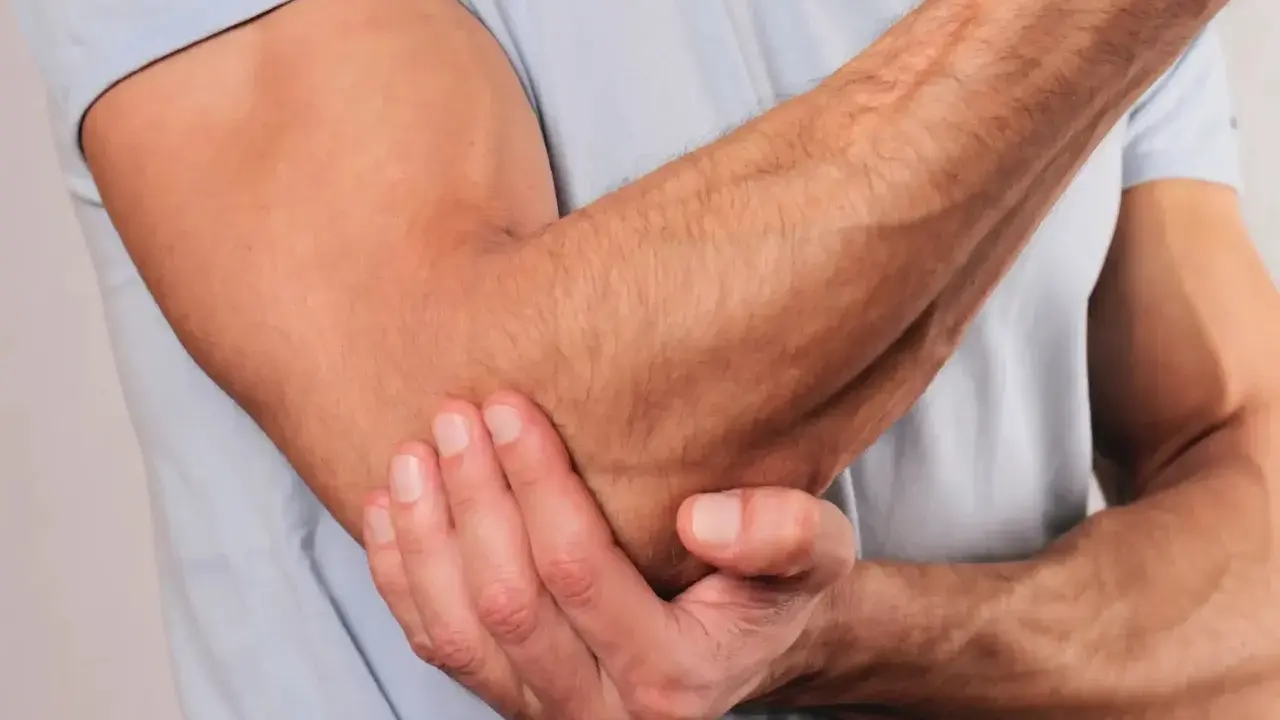 En person håller om sin armbåge, som om den har ont i armbågen.