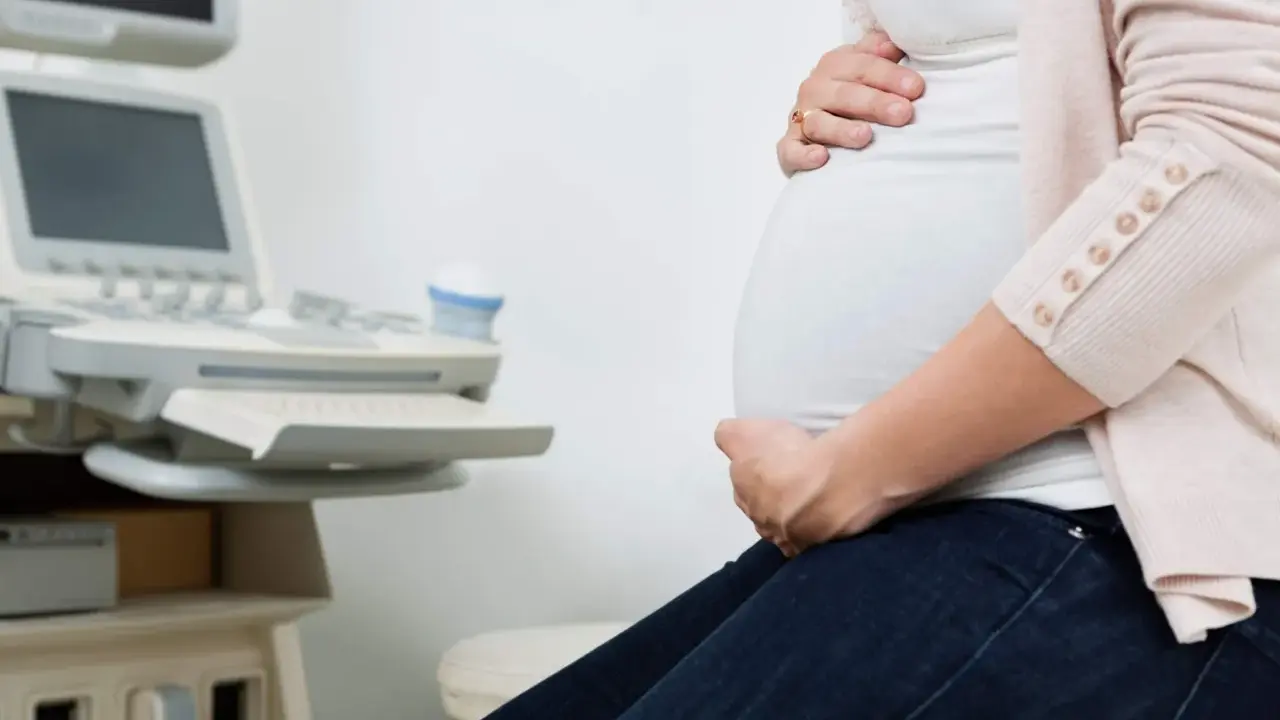 Gravid kvinna med händer på magen vid en ultraljudsapparat. Hon väntar på besked om moderkakan lossnar.