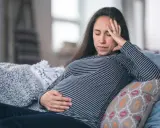Gravid kvinna med ont i magen på natten, vilar på en soffa med handen på magen och pannan.