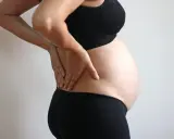 Gravid kvinna med händerna på ryggen, upplever smärta som kan liknas vid analkramp.