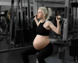 En **spinning gravid** tränar på gym. Hon sitter på en träningsmaskin och drar i ett handtag.