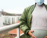 Gravid kvinna med munskydd på balkongen, omgiven av stadens silhuett. Känns det som att du är oftare sjuk gravid?