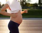 En gravid kvinna springer på en löparbana i solnedgången, med hörlurar i öronen.