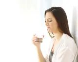 Kvinna med grimaserande ansikte håller ett glas vatten, möjligen ett symptom på oral galvanism.