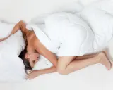 Klarvaken mitt i natten, gravid kvinna i fosterställning under ett vitt täcke.