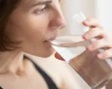 Kvinna dricker vatten för att lindra muntorrhet, en potentiell biverkning av cancerbehandling.