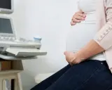 Gravid kvinna med händer på magen vid en ultraljudsapparat. Hon väntar på besked om moderkakan lossnar.