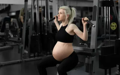En **spinning gravid** tränar på gym. Hon sitter på en träningsmaskin och drar i ett handtag.