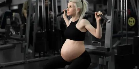 En **spinning gravid** tränar på gym. Hon sitter på en träningsmaskin och drar i ett handtag.