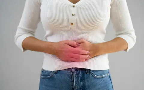 Kvinna håller sig om magen med en röd glöd som indikerar smärta, möjligen relaterat till pelvic congestion syndrome svenska.