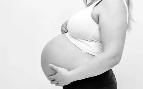 Gravid mage med händer som stöttar. Kanske ont i ljumsken gravid?