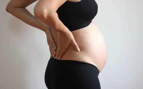 Gravid kvinna med händerna på ryggen, upplever smärta som kan liknas vid analkramp.