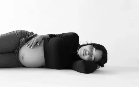 Gravid kvinna ligger på rygg, med handen på sin mage. Hon ser ut att vila.