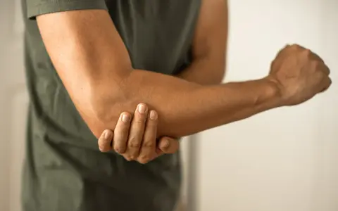 Person håller om sin armbåge, som om den har ett avslitet ledband.