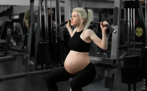 En **spinning gravid** tränar på gym. Hon sitter på en träningsmaskin och drar i ett handtag.