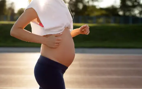 En gravid kvinna springer på en löparbana i solnedgången, med hörlurar i öronen.