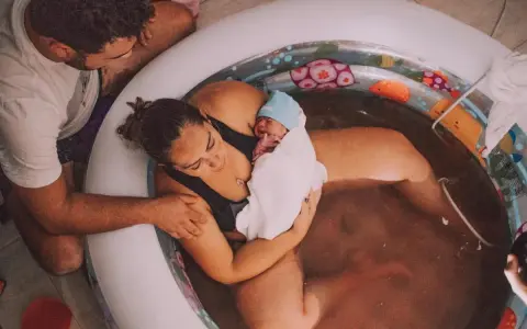 En nyfödd bebis vilar i sin mammas famn i ett födelsekar. Pappan stöttar dem båda. En lycklig stund för familjen som väntade sitt andra barn.