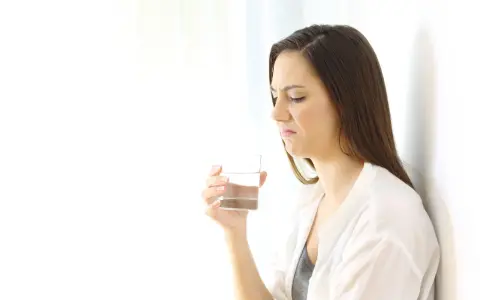 Kvinna med grimaserande ansikte håller ett glas vatten, möjligen ett symptom på oral galvanism.
