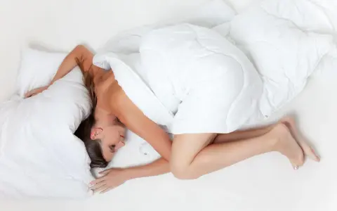 Klarvaken mitt i natten, gravid kvinna i fosterställning under ett vitt täcke.