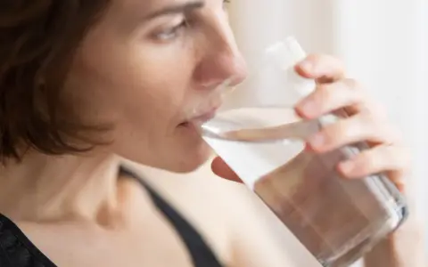 Kvinna dricker vatten för att lindra muntorrhet, en potentiell biverkning av cancerbehandling.