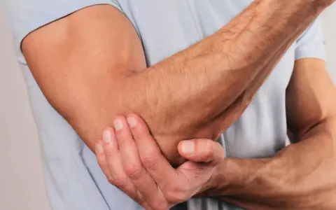 En person håller om sin armbåge, som om den har ont i armbågen.