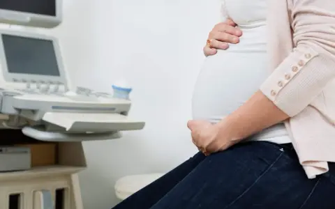 Gravid kvinna med händer på magen vid en ultraljudsapparat. Hon väntar på besked om moderkakan lossnar.