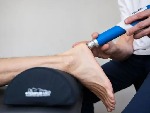 Behandling av plantar fasciit med stötvågsbehandling. En terapeut använder en blå enhet för att behandla en fot.