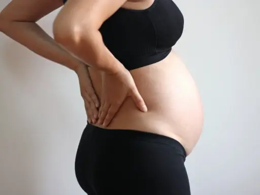 Gravid kvinna med händerna på ryggen, upplever smärta som kan liknas vid analkramp.