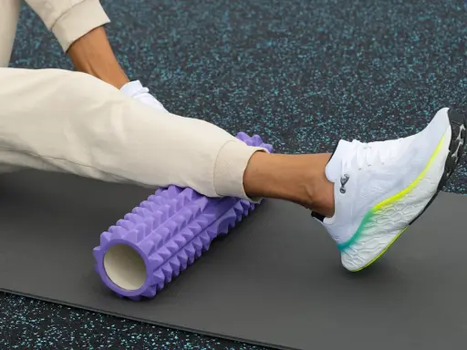 Person använder en lila foam roller rygg för att stretcha benet på en träningsmatta.