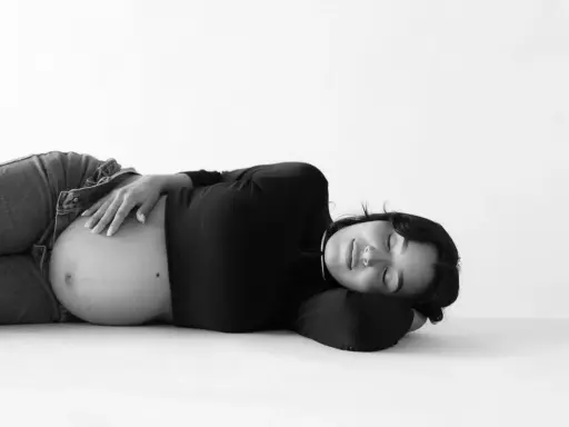Gravid kvinna ligger på rygg, med handen på sin mage. Hon ser ut att vila.