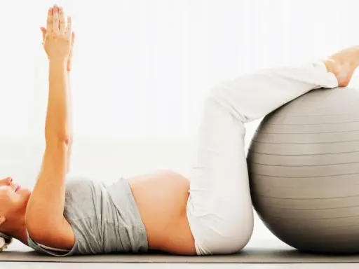Gravid kvinna tränar magmuskler med en pilatesboll.