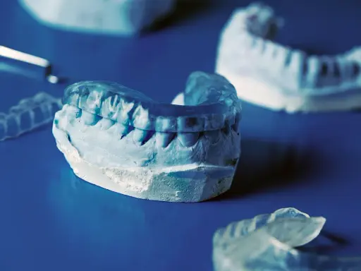 Tandläkarmodeller visar en bettskena för barn, gjord av genomskinligt plastmaterial, som passar över en gipsavgjutning av tänder.