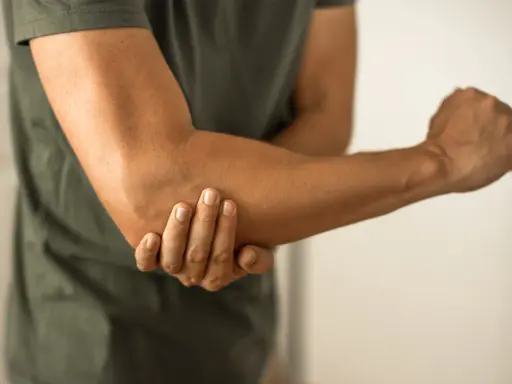 Person håller om sin armbåge, som om den har ett avslitet ledband.