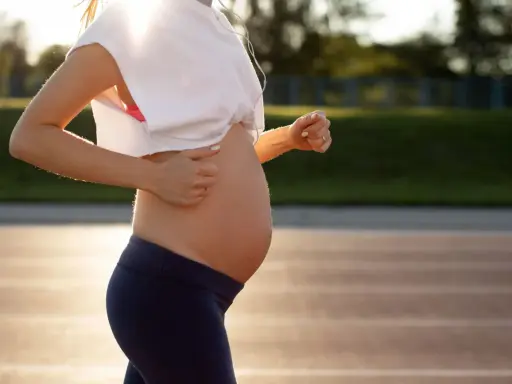 En gravid kvinna springer på en löparbana i solnedgången, med hörlurar i öronen.