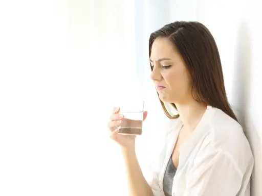 Kvinna med grimaserande ansikte håller ett glas vatten, möjligen ett symptom på oral galvanism.