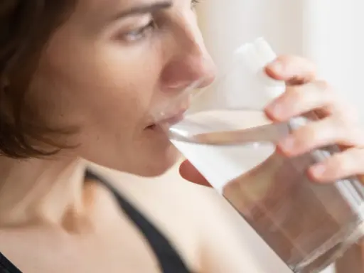 Kvinna dricker vatten för att lindra muntorrhet, en potentiell biverkning av cancerbehandling.