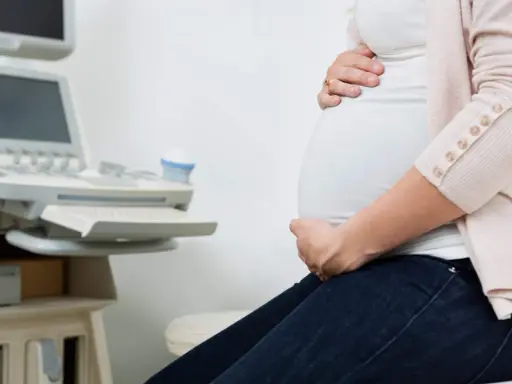 Gravid kvinna med händer på magen vid en ultraljudsapparat. Hon väntar på besked om moderkakan lossnar.