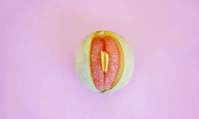 En melon delad på mitten, med en bit av en annan frukt inuti. Kan liknas vid ett svullet underliv, kanske som en graviditet kan kännas.