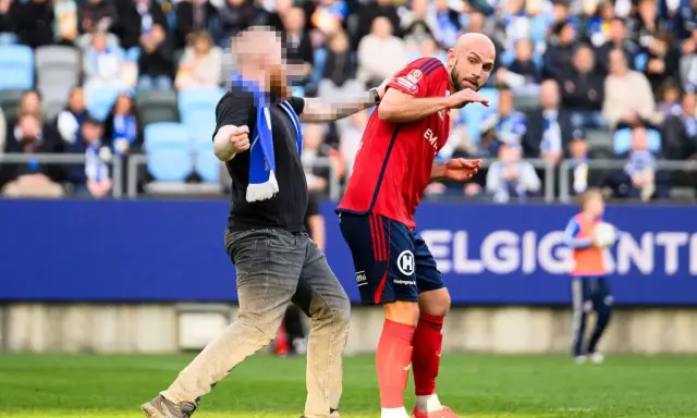 En åskådare ger en fotbollsspelare ett hårt slag mot hakan på planen.
