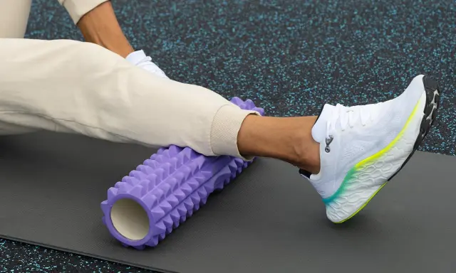 Person använder en lila foam roller rygg för att stretcha benet på en träningsmatta.