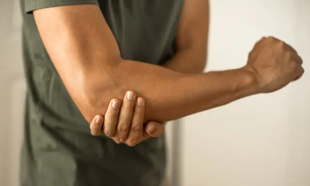 Person håller om sin armbåge, som om den har ett avslitet ledband.