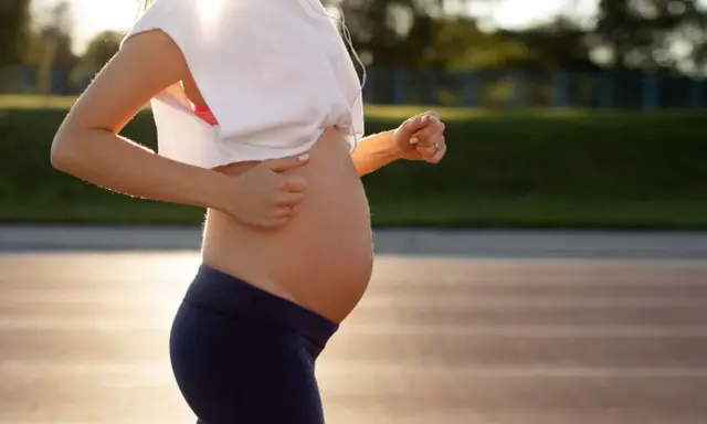 En gravid kvinna springer på en löparbana i solnedgången, med hörlurar i öronen.